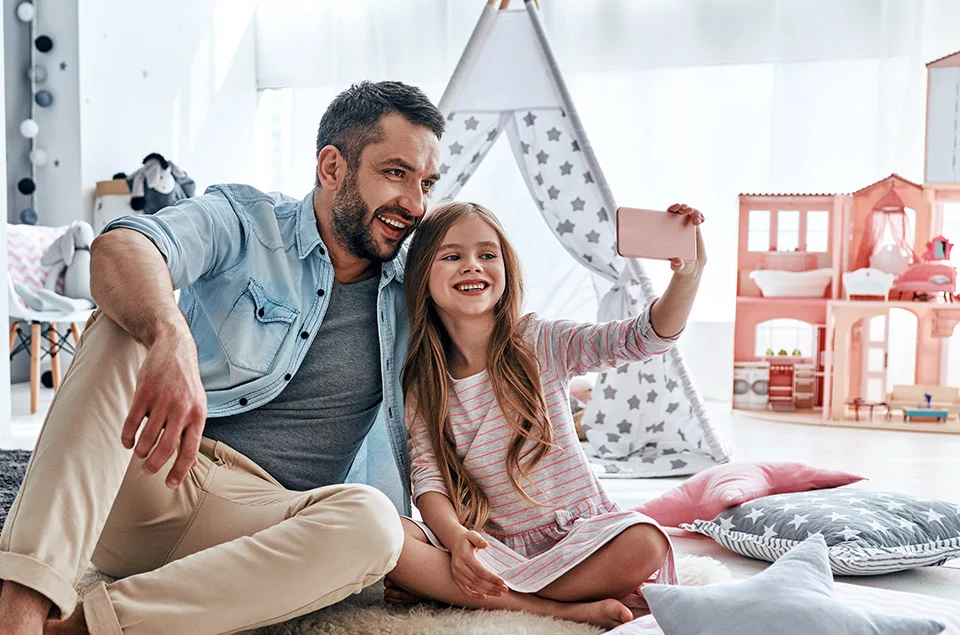 Vater und Tochter sitzen im Kinderzimmer auf dem Boden und machen ein Selfie