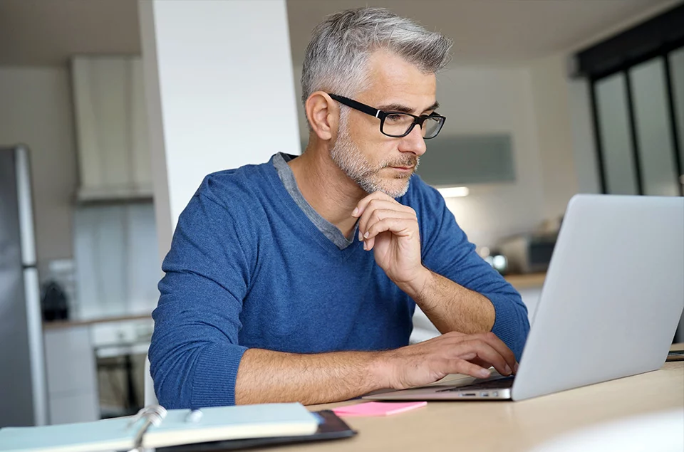 Ein Mann sitzt an einem Tisch und schaut auf seinen Laptop