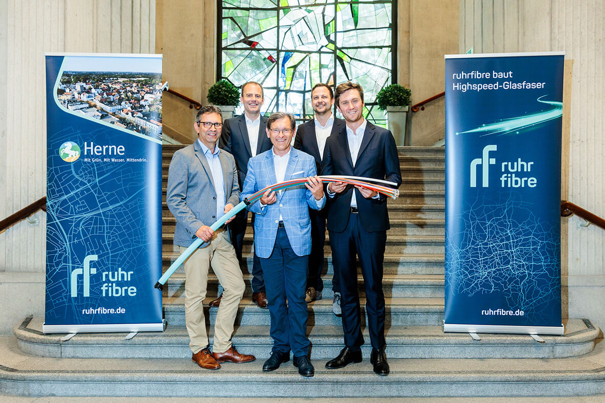 Fünf Männer stehen auf einer Treppe zwischen zwei Ruhrfibre Plakaten und halten Glasfaser